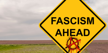 A field in the background with a yellow road sign that says "Fascism Ahead" and at the bottom of the sign is a anarchy symbol - a red A in a circle.